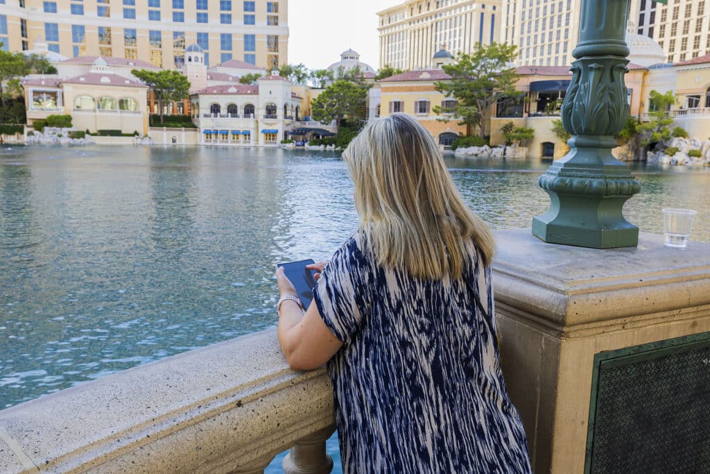 Close up view of woman on embankment surfing on mobile. Blue water surface and  buildings on background. Las Vegas, Nevada, USA.